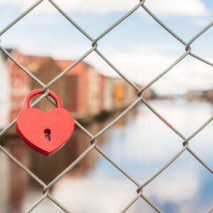 Cadenas rouge en forme de coeur accroché à un grillage symbolisant relations malsaines et enfermantes