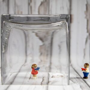 Personnage lego sous un verre, isolé d’un autre : image de l'isolement causé par une personne manipulatrice et perverse