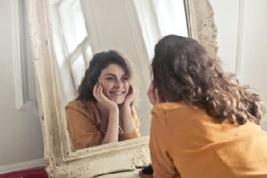 Une jeune femme se regarde dans un miroir en souriant, elle est heureuse, car a une bonne estime de soi