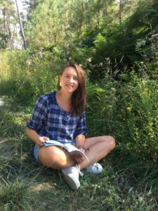 Photo de Julie, assise au sol et lisant un livre dans les bois