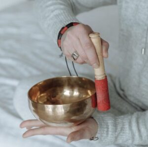 Une personne fait sonner un bol tibétain sur le creux de sa main avec un maillet