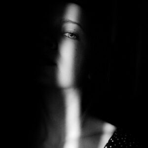 Visage d’une femme caché dans l’ombre, seul un œil éclairé apparaît, évoquant une faible estime de soi